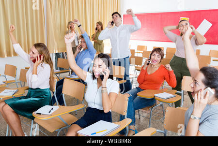 Group of adult happy cheerful positive smiling students expressing happiness while talking on phones after passing exam in class Stock Photo