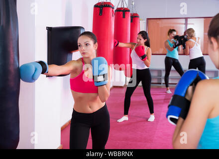 Active female is doing exercises with punching bag in sporty gym. Stock Photo