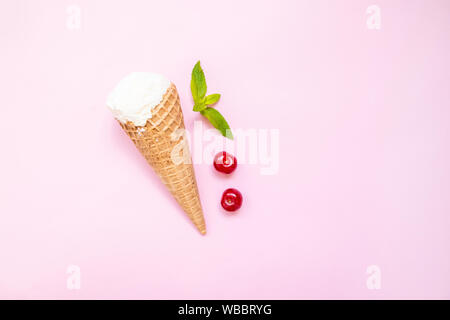 Mint vanilla ice cream with in a waffle cone with mint leaves and ripe cherry berries on a pink plain background. Stock Photo
