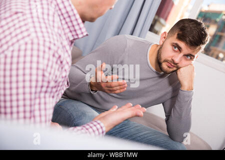 Upset man having unpleasant talk with male colleague on couch in home interior Stock Photo
