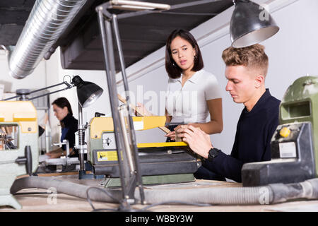 Female student creating training architectural model together with her friend working on scroll saw in university workshop Stock Photo
