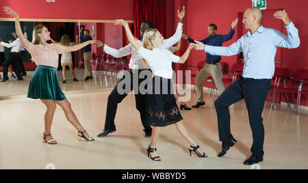 Young smiling people practicing vigorous jive movements in dance class Stock Photo