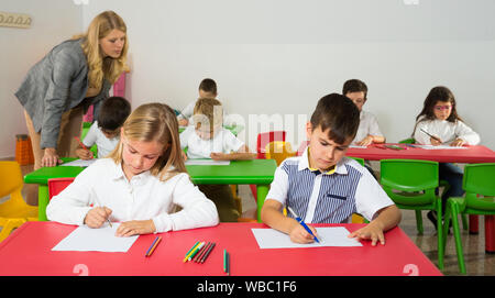 Little diligent schoolkids and their female teacher working at classroom Stock Photo
