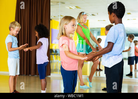 Group of preteen boys and girls training movements of slow foxtrot in dance studio with female coach Stock Photo