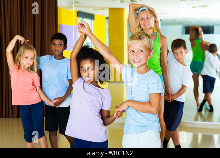 Group of preteen children training movements of slow foxtrot in dance studio with female coach. Focus on girl Stock Photo