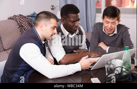 Cheerful male friends using laptop during bachelor gathering at home Stock Photo