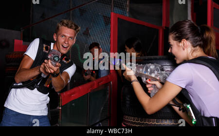 Positive guy holding colored laser guns and took aim during laser tag game in labyrinth Stock Photo