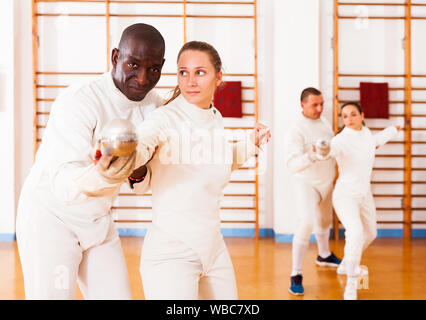 Female fencer practicing  movements with african american male trainer at workout Stock Photo