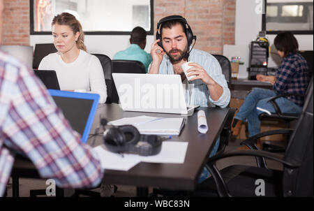 Latin hipster guy attentively watching webinar online using headset in modern coworking space Stock Photo