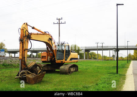 excavator standing on side of a road Stock Photo