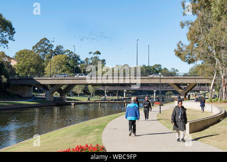 People walk along the Foreshore Reserve beside the Parramatta River towards the 1975 built Barry Wilde Bridge in Parramatta, Sydney Australia Stock Photo