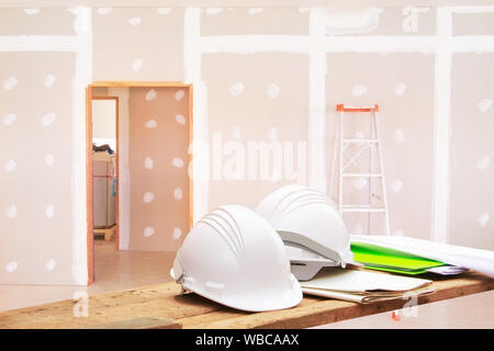 white safety helmet plastic white paper blueprint on Wooden floor in room work gypsum board wall interior decoration of home construction site Stock Photo
