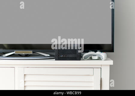Flat LCD television on white cabinet in the living room with dark gray wall. Video gaming console and gamepad. Gamer station mockup Stock Photo