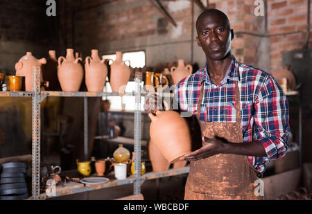 Smiling African American potter proffering clay goods he created in pottery shop Stock Photo