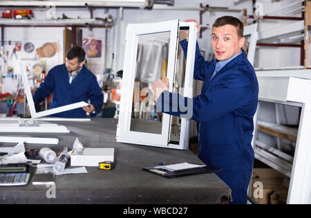 Two smiling cheerful positive careful workmen inspecting PVC manufacturing output in workshop Stock Photo