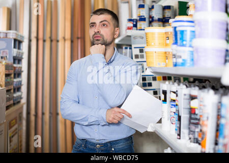 Man is selecting paint for repair with shop list in the store. Stock Photo