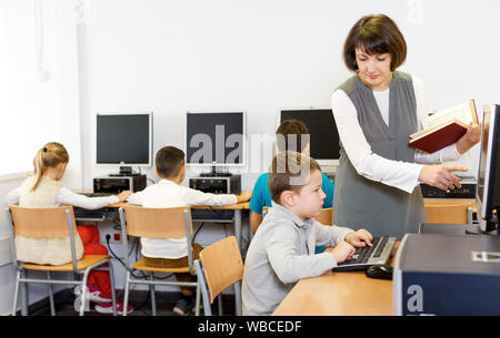 Friendly woman teacher helping tween boy during lesson in computer room of school library Stock Photo