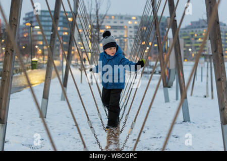 Young boy climbing and holding balance on a snowy playground in the winter time. Stock Photo