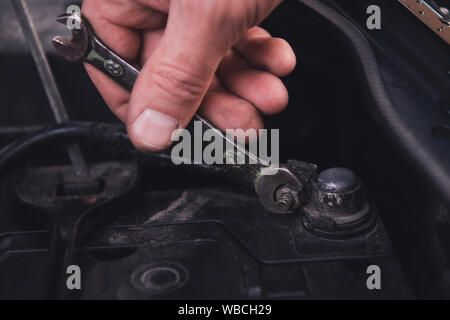 Man's hand tightens the nut with an old wrench. Battery replacement at the garage. Closeup. Stock Photo