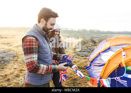 Happy young couple dressed in warm clothes pitching a tent at the field Stock Photo