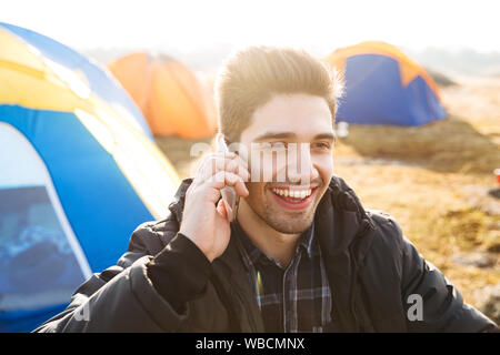 Handsome cheerful man camping outdoors, talking on mobile phone Stock Photo
