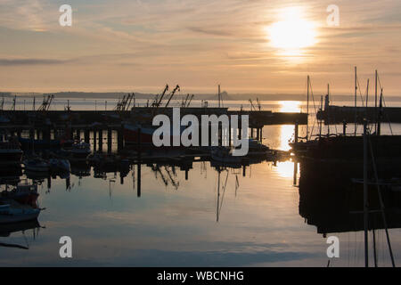 Silhouettes of boats in Newlyn Harbour, Cornwall, at sunrise with St Michael's Mount in background Stock Photo