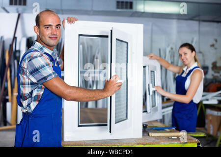 Diligent efficient positive confident man in workwear with finished window from pvc profile at workplace Stock Photo