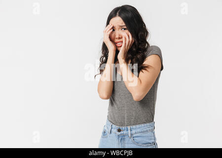 Image of terrified brunette woman 20s dressed in basic clothes grabbing her face in fright isolated over white background Stock Photo