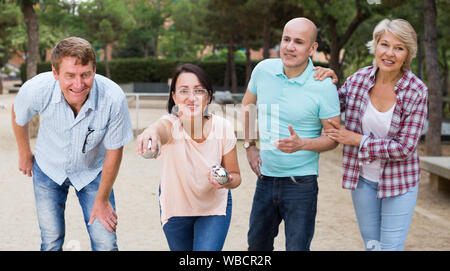 Cheerful males and females playing petanque in park on holidays Stock
