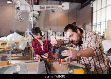 Young handsome bearded man enjoying his hobby - modeling light airplanes in aircraft hangar Stock Photo