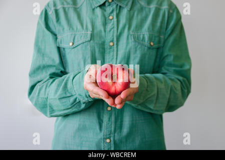 Man in green shirt with heart shaped peach in his hands Stock Photo