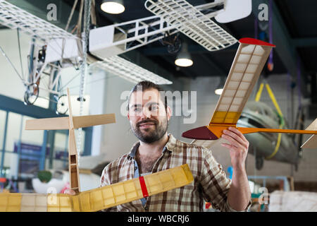 Portrait of happy male hobbyist with monoplane models he created in aircraft workshop Stock Photo