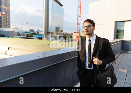 Handsome confident young businessman wearing suit walking outdoors at the city streets Stock Photo