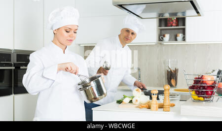 Man cook and woman standing with whisk, professional chefs in uniform working on kitchen Stock Photo