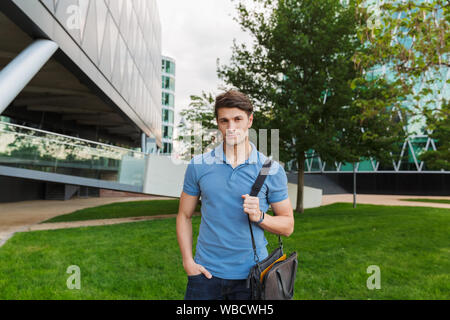 Handsome young man dressed casually spending time outdoors at the city, carrying bag Stock Photo