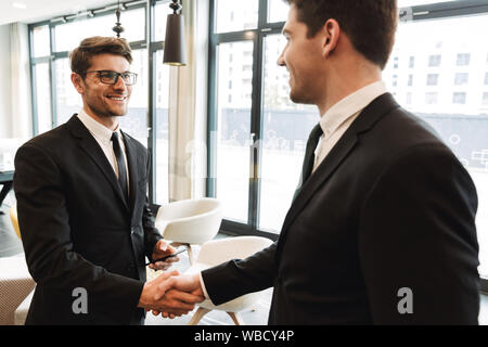 Photo of a businessmen colleagues indoors in business center office using mobile phone shaking hands. Stock Photo