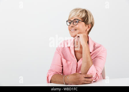 Portrait closeup of positive middle-aged woman with short blond hair smiling while sitting at table isolated over white background Stock Photo