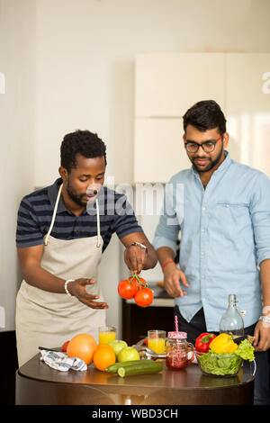 Shot of two male friends preparing vegetable salad in kitchen. Multi ethnic students cooking dinner together in hostel. Dieting, vegetarianism concept Stock Photo