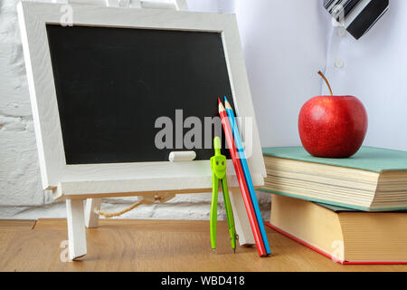 School supplies, miniature chalk board, a stack of books and apple on the table, soft focus Stock Photo
