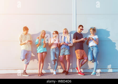 Group of young friends using their mobile phones in front of a wall Stock Photo
