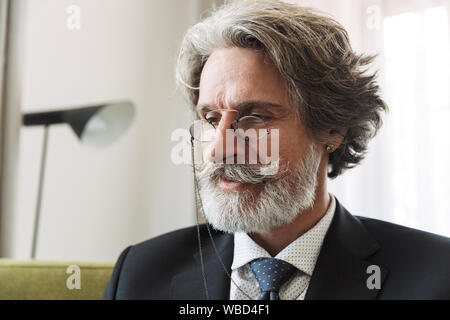 Image of a serious handsome grey-haired senior businessman indoors at home dressed in formal clothes wearing glasses. Stock Photo