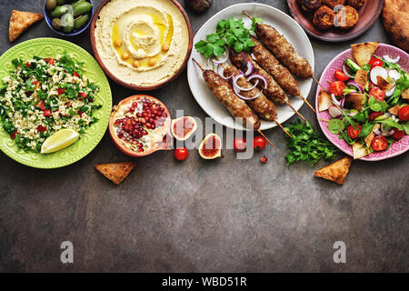 Assorted Middle Eastern and arabic dishes on a dark rustic background. Hummus,tabbouleh, salad Fattoush,pita,meat kebab,falafel,baklava,pomegranate. H