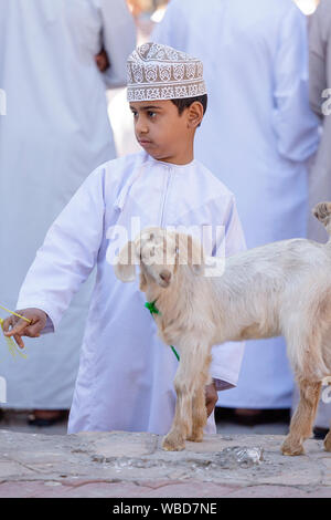 Young boy in traditional clothes with a baby goat at cattle market, Nizwa, Sultanate of Oman Stock Photo