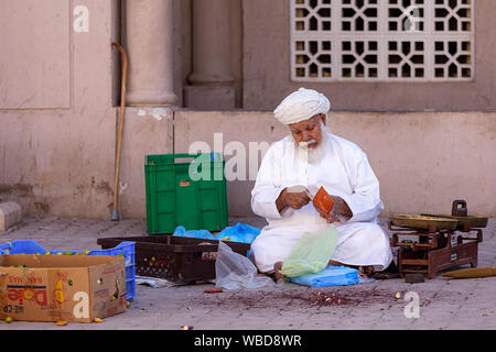 Man sitting on the floor by the produce he sells and a scale, counting money from wallet at cattle market, Nizwa, Sultanate of Oman Stock Photo