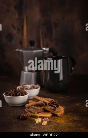 Cinnamon sticks, anise stars, caramelized sugar, coffee pot and milk jug on a dark background Stock Photo