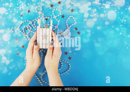 Christmas decoration on the Christmas tree in the form of small white wooden sledges in female hands on a blue background Stock Photo