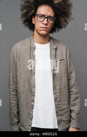 photo of a young curly sad teenage guy posing isolated over grey wall background wbde2g