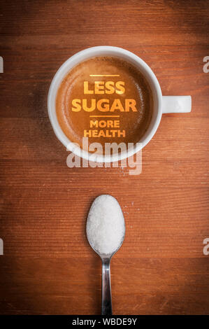 Health care concept: a coffee cup with text less sugar more health on wooden table and a spoon full of white sugar Stock Photo