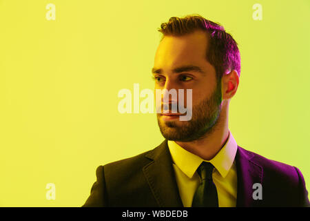 Image of serious young businessman in formal suit posing at camera isolated over yellow background Stock Photo