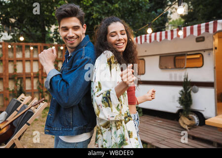 Portrait of funny couple man and woman smiling while dancing together near house on wheels outdoors Stock Photo